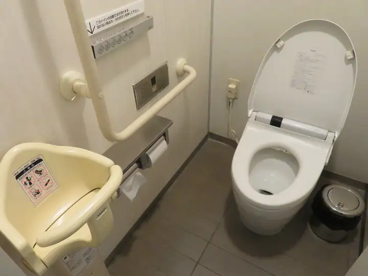 洋式便器の向かい側の壁に設置された幼児用ベビーチェアと手すり