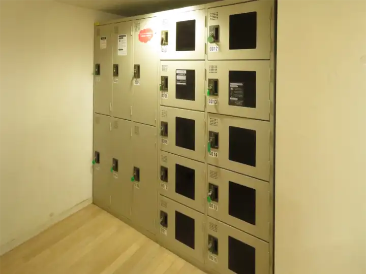 階段下などの壁際に並んで設置された、ベージュ色の大小さまざまなサイズのコインロッカー