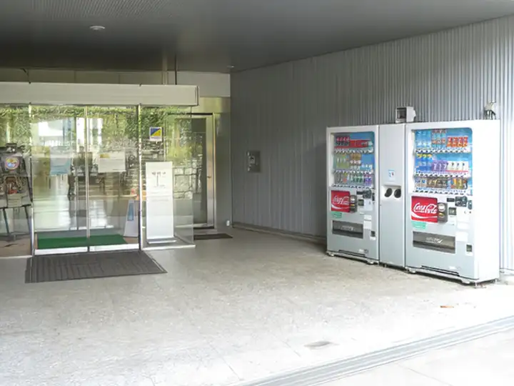 施設入り口の自動ドア横にある、屋根付きの屋外スペースに設置された3台の飲料自動販売機